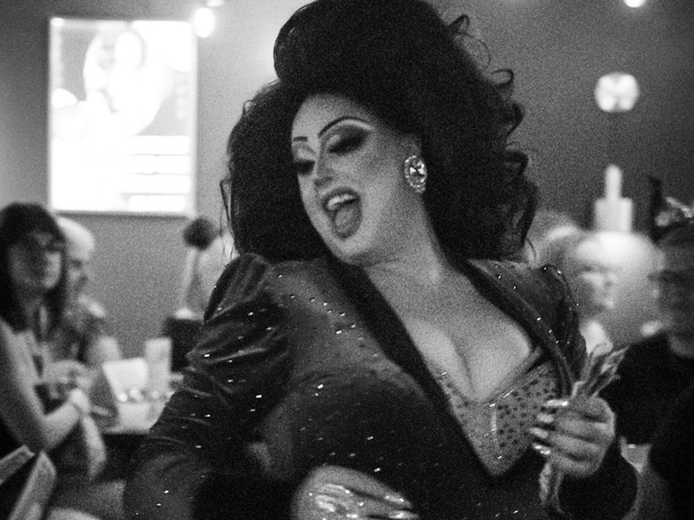 Queen mid‑lip sync with neon lights behind